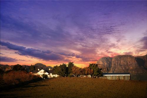 帕尔Bakenhof Winelands Lodge的一座在田野上的建筑,背景是日落