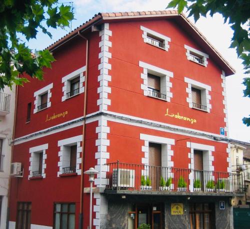 FuenmayorHostal Labranza的红色的建筑,设有窗户和阳台