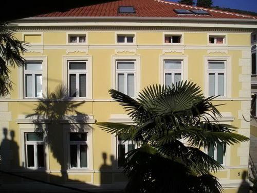 奥帕提亚Apartment Damir的一座黄色的建筑,前面有棕榈树