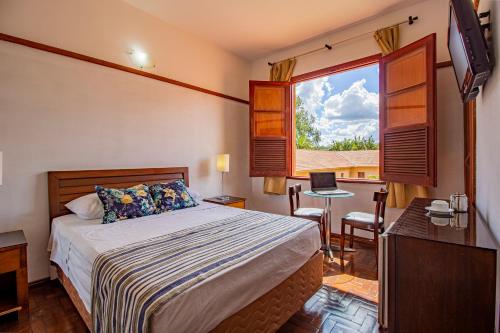 阿拉沙Hotel Nacional Inn Araxá Previdência的一间卧室配有一张床、一张书桌和一个窗户。