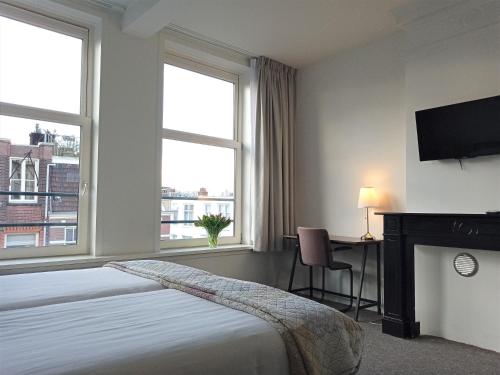 阿姆斯特丹威尔第酒店的一间卧室配有一张床、一张书桌和两个窗户。