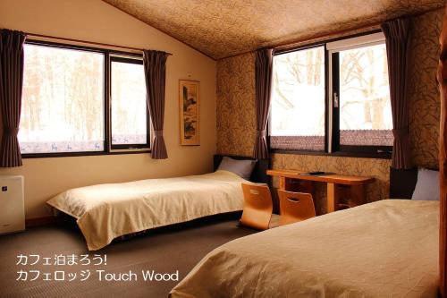 美瑛町カフェロッジ Touch Wood的客房设有两张床、一张桌子和两个窗户。