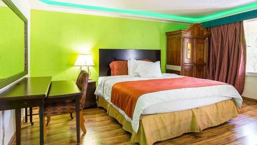 小石城Magnuson Hotel Little Rock South的一间卧室配有一张带书桌的床和绿色的墙壁