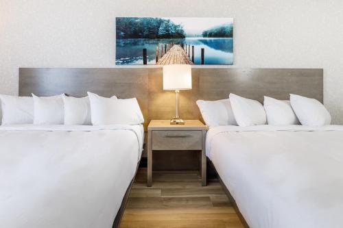 魁北克市Repotel Henri IV Québec的两张位于酒店客房的床铺,旁边是一张桌子和灯