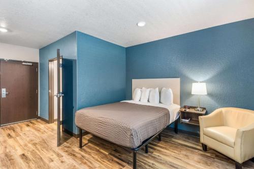 布雷登顿WoodSpring Suites Bradenton的一间卧室配有一张床、一把椅子和蓝色的墙壁