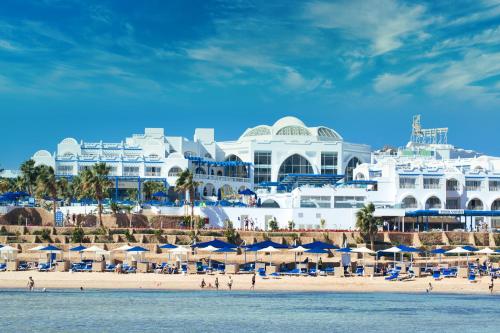 沙姆沙伊赫Pickalbatros Palace Sharm - "Aqua Park"的一个带遮阳伞的海滩和一座白色的大建筑