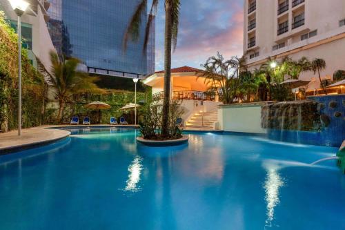 韦拉克鲁斯Ramada Plaza by Wyndham Veracruz Boca del Rio的一座种植了棕榈树的大型蓝色游泳池和一座建筑