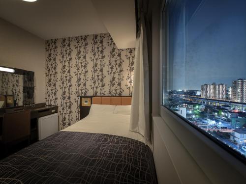 古河市APA Hotel Ibaraki Koga Ekimae的一间卧室设有一张床和一个享有城市美景的窗户