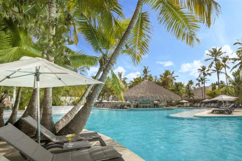 蓬塔卡纳蓬塔卡纳加泰罗尼亚全包酒店的一个带椅子和遮阳伞的游泳池以及棕榈树