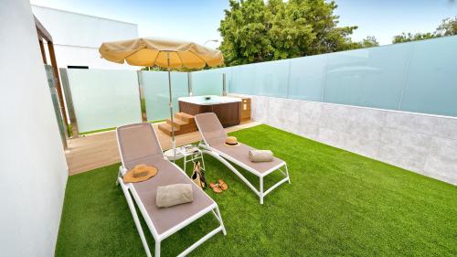 马斯帕洛马斯Club Maspalomas Suites & Spa - Adults Only的天井配有两把椅子和一把遮阳伞,位于草地上