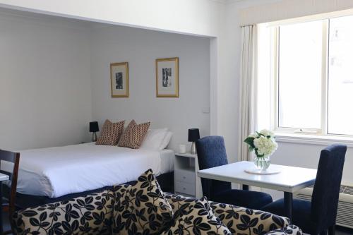 墨尔本Hotel Collins的卧室配有1张床、1张桌子和1张桌子以及椅子。