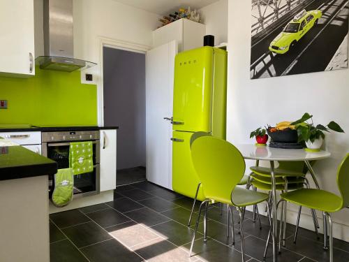 伦敦3 bed Apartment in Colliers Wood的厨房配有绿色橱柜和一张带绿色椅子的桌子