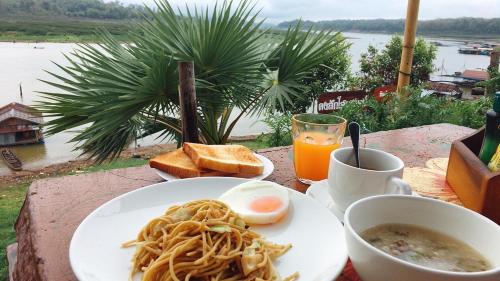 桑卡武里Baan Dongsak River view的一张桌子,上面放着一盘意大利面、鸡蛋和饮料