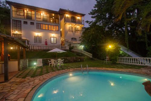 欧鲁普雷图Hotel Pousada Arcádia Mineira的夜间在房子前面的游泳池