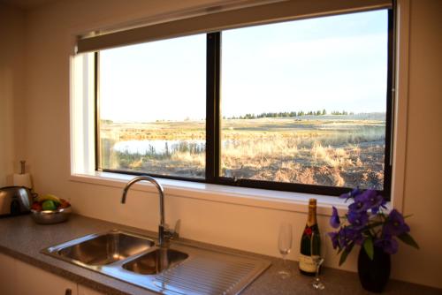 特卡波湖Tekapo Luxury Apartments的厨房水槽和享有田野景致的窗户
