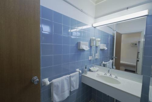 昆比恩奥林匹亚汽车旅馆的蓝色瓷砖浴室设有水槽和镜子