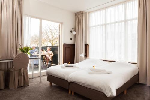 阿尔克马尔斯坦德恩兰德酒店的一间卧室配有一张大床和一张桌子,其中一人坐在椅子上