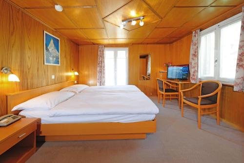 采尔马特阿尔夫贝尔酒店的一间卧室配有一张床、一张书桌和一台电视