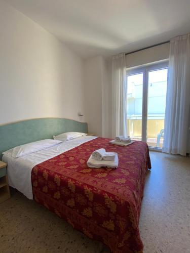 里米尼阿泰德酒店的一间卧室配有一张带红色毯子的床和窗户。