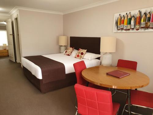 塔姆沃思The Aston Motel Tamworth的一间卧室配有一张床和一张桌子及红色椅子