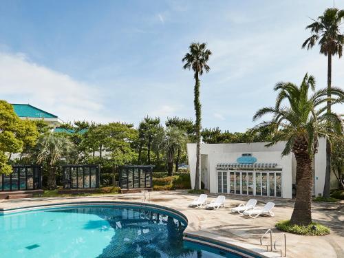 西归浦市Bloom Hotel的一座建筑前的游泳池,里面设有椅子和棕榈树