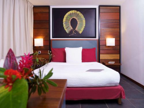库鲁Hotel Mercure Kourou Ariatel的酒店客房配有一张带红色枕头和羽绒被的床。