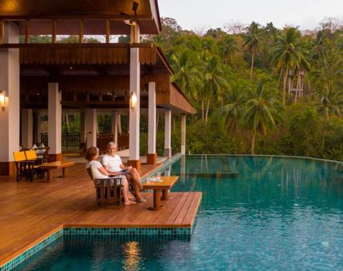 布莱尔港Symphony Samudra Beachside Jungle Resort And Spa的两人坐在游泳池旁的甲板上