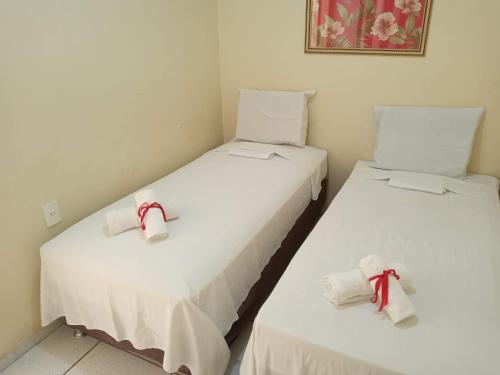 北茹阿泽鲁Pousada Aconchego的配有白色床单和红色弓的客房内的两张床