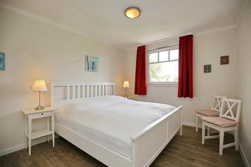 博尔滕哈根Reethaus Am Mariannenweg 15b的卧室配有白色大床和红色窗帘
