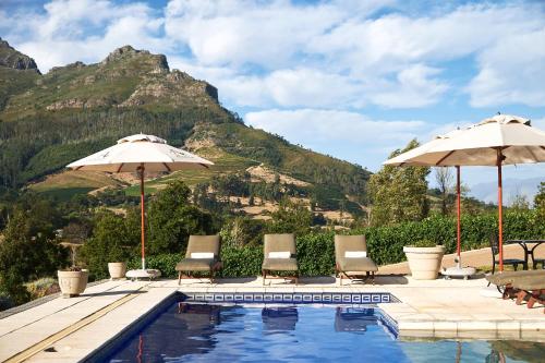 斯泰伦博斯Alluvia Boutique Winery & Luxury Accommodation的一个带椅子和遮阳伞的游泳池以及山地