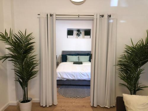 特拉维夫Villa Tlv רחוב הירקון 27 תל אביב的一间卧室配有带白色窗帘和2种植物的床