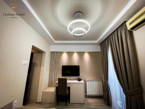 波德戈里察Hotel Holiday的客房设有一张书桌、一台电视和吊灯。