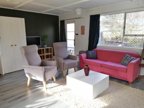 上哈特Cozy guesthouse at the Rabbithole, Akatarawa Valley的客厅配有红色的沙发和两把椅子