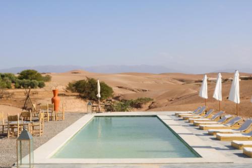 El KariaEmeraude Camp Agafay的沙漠中的游泳池,配有椅子和遮阳伞
