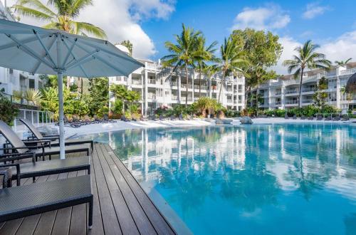 棕榈湾Beach Club Palm Cove 2 Bedroom Luxury Penthouse的一座带遮阳伞和椅子的游泳池以及大楼
