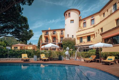 曼德琉-拉纳普勒Ermitage de l'Oasis & Spa - Cannes Mandelieu的一座带椅子和遮阳伞的大楼前的游泳池