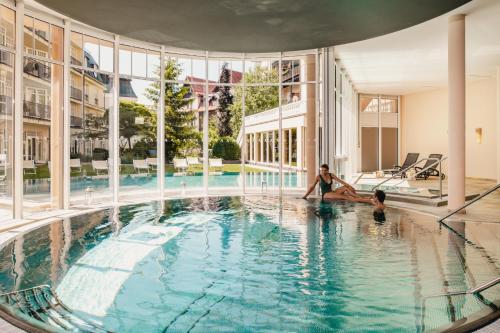 玛丽亚温泉Falkensteiner Spa Resort Marianske Lazne的一名妇女和两名儿童坐在建筑物的游泳池里