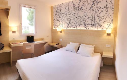 里沃萨尔特Kyriad Direct Perpignan - Aeroport的卧室配有白色的床、书桌和窗户。