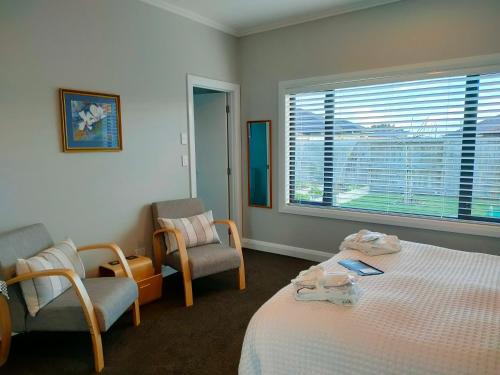 陶波Stay Taupo的一间卧室配有一张床、两把椅子和一个窗户