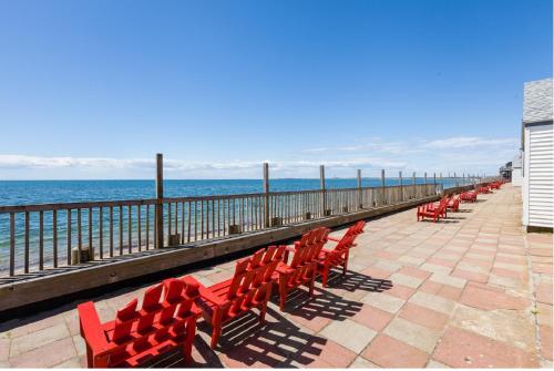 北特鲁罗Oceana Cottages的坐在靠近大海的码头上的一排红色椅子
