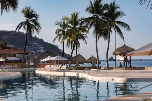 伊斯塔帕伊斯塔帕全包假日酒店度假村的一个带椅子和棕榈树的游泳池以及大海
