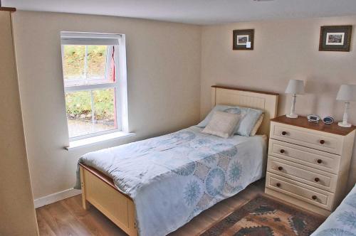 格伦贝赫Glenbeigh Holiday Cottage - Tigin Mamo的一间卧室配有带梳妆台和窗户的床。
