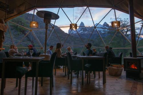厄尔查尔坦巴塔哥尼亚生态圆顶豪华帐篷的餐厅,有坐在大窗户前的桌子旁的人