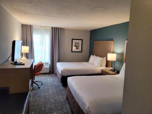 亚历山德里亚Comfort Inn & Suites Alexandria West的酒店客房设有两张床、一张桌子和一台电视。