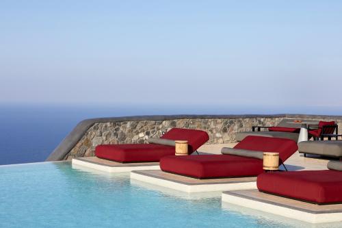 易莫洛林White Pearl Cavalieri的水边的游泳池配有红色枕头和椅子