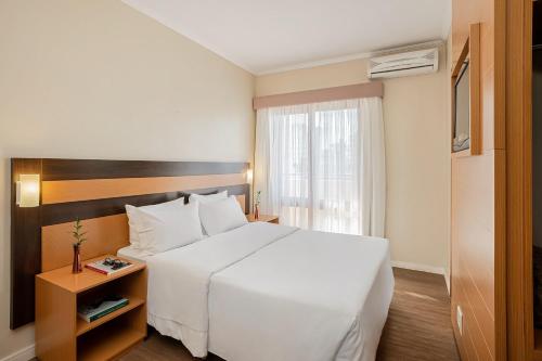 阿雷格里港Piazza Navona Porto Alegre by Intercity的酒店客房设有一张白色大床和一个窗户。