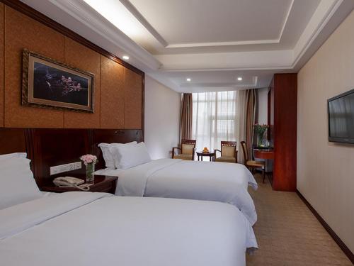 龙岗维也纳酒店深圳坪地店的一间酒店客房,设有两张白色的床和窗户。