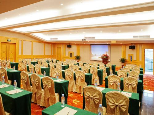 深圳维也纳国际酒店深圳大梅沙店的宴会厅配有绿色桌椅和屏幕