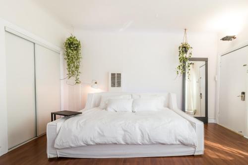洛杉矶Sunny Boho Chic West Hollywood Flat!的白色卧室配有白色床,墙上挂着植物