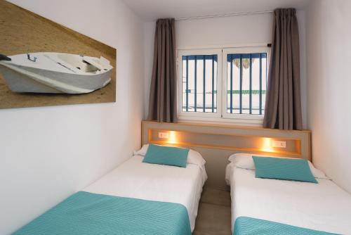 卡门港Apartamentos Playamar的窗户上设有船只的客房内的两张床